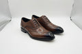 Brown dress shoe held by a hand with a brand box in the background