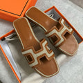 Brown and beige sandals with a geometric design in an open orange box.