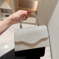 Hand holding a silver glittery handbag with a beige stripe against a neutral background