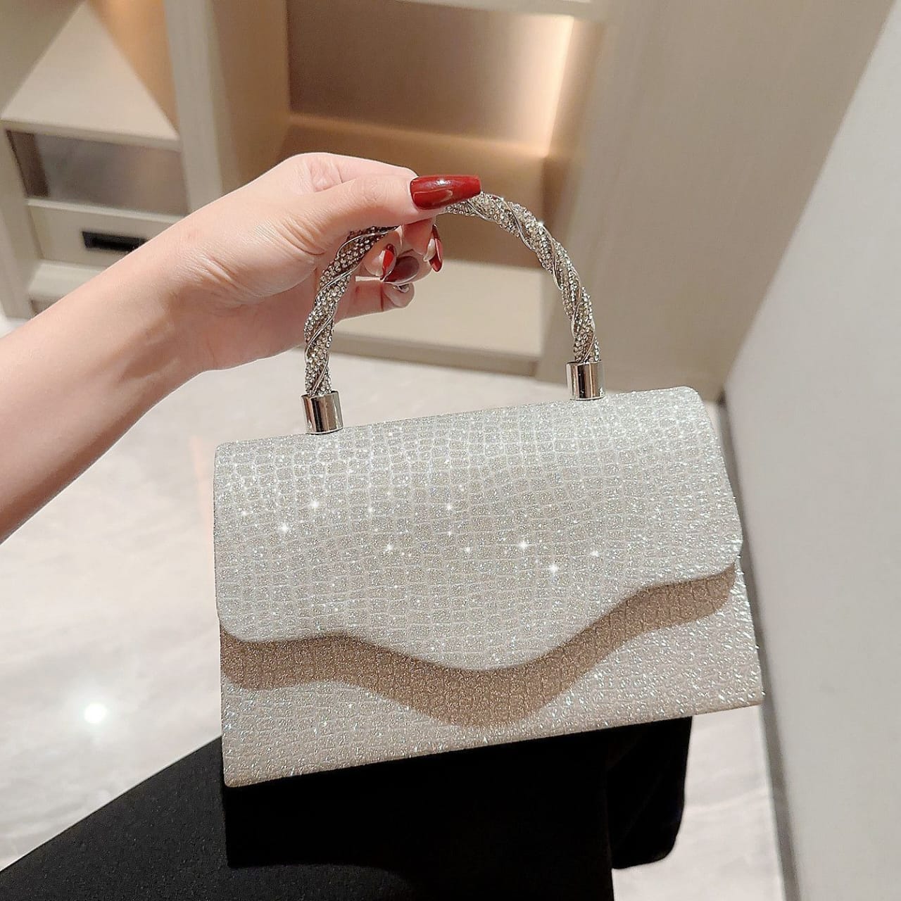 Hand holding a silver glittery handbag with a beige stripe against a neutral background