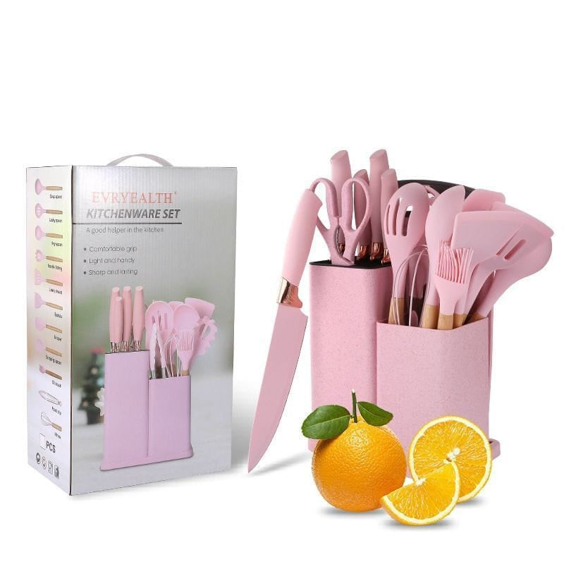 Pink kitchen utensil set with packaging and oranges on a white background