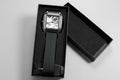Black wristwatch with a white face in a black box held by a hand on a dark gray background