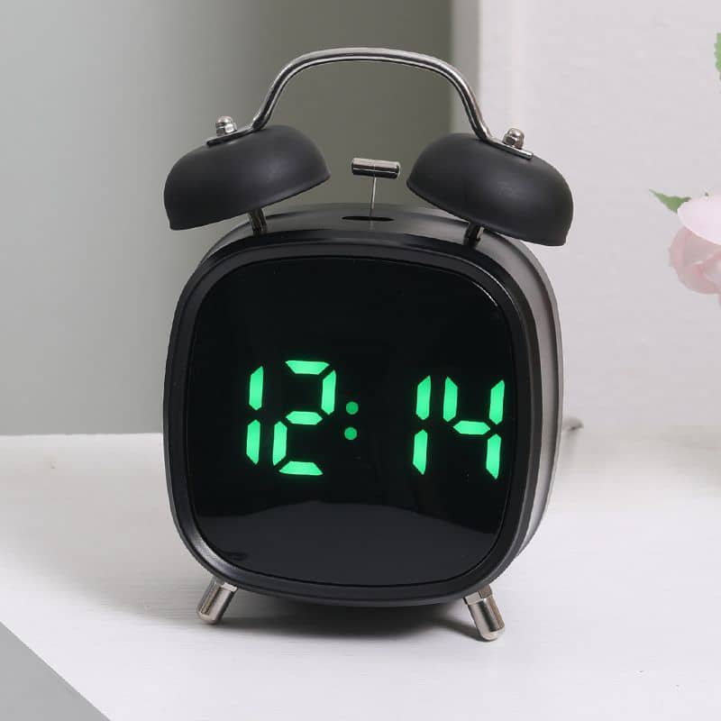 Black digital alarm clock with green LED display on a white surface.